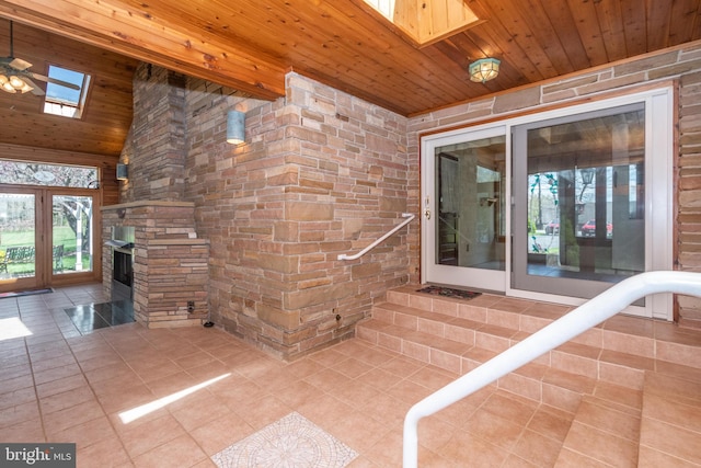 interior space with a stone fireplace, wooden ceiling, ceiling fan, and a skylight