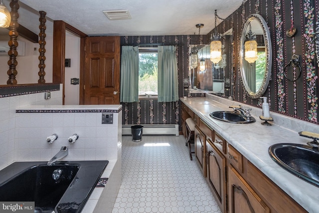 bathroom with tiled bath, dual vanity, a baseboard radiator, a textured ceiling, and tile patterned flooring