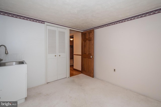 unfurnished bedroom featuring carpet, sink, a textured ceiling, and a closet