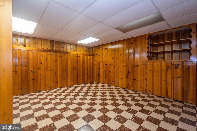 basement featuring wood walls, a drop ceiling, and light tile patterned floors