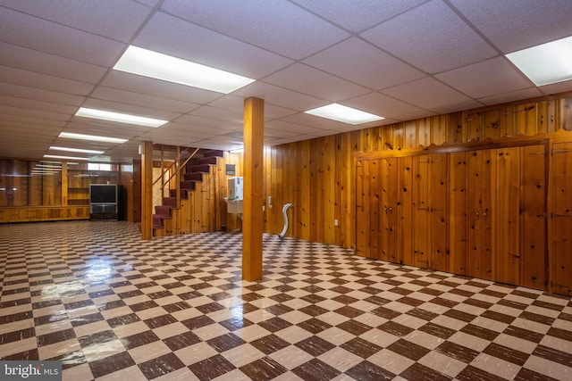 basement featuring wood walls and a drop ceiling