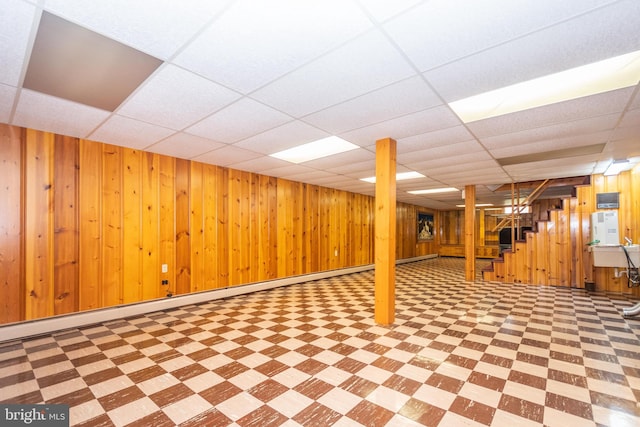 basement featuring wood walls, a drop ceiling, light tile patterned floors, and baseboard heating