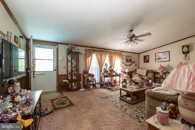 living room featuring carpet, a textured ceiling, ceiling fan, crown molding, and wood walls