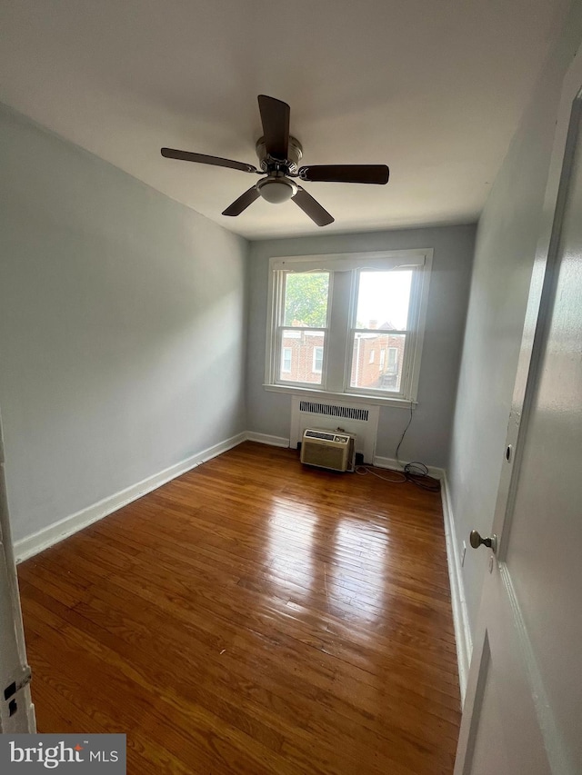 spare room with ceiling fan, radiator, wood-type flooring, and a wall unit AC