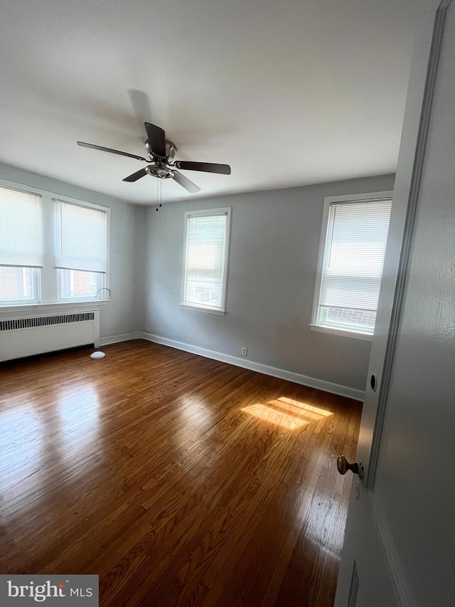 empty room featuring dark hardwood / wood-style floors, ceiling fan, and radiator heating unit