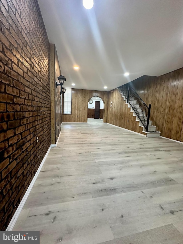 interior space featuring light wood-type flooring, wood walls, and brick wall