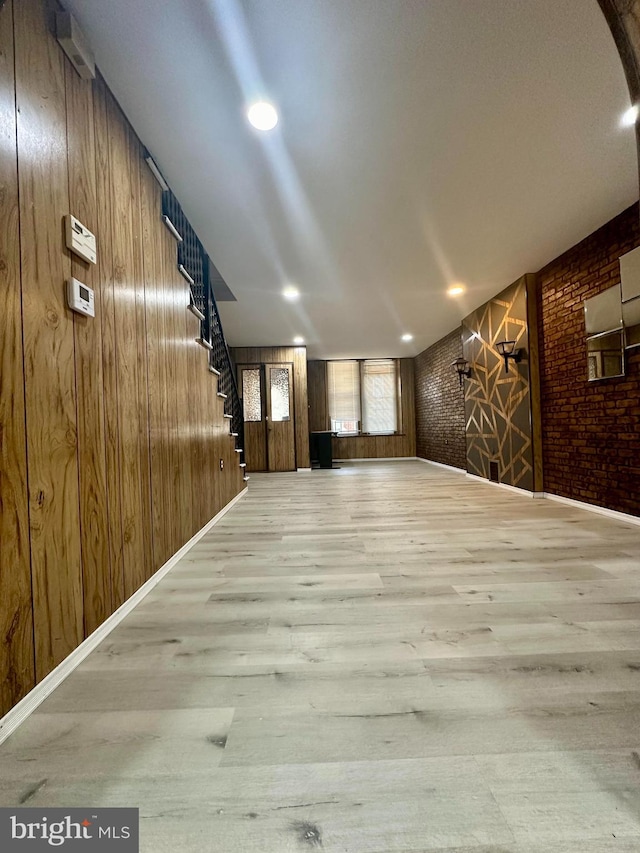 corridor with wooden walls, light hardwood / wood-style floors, and brick wall