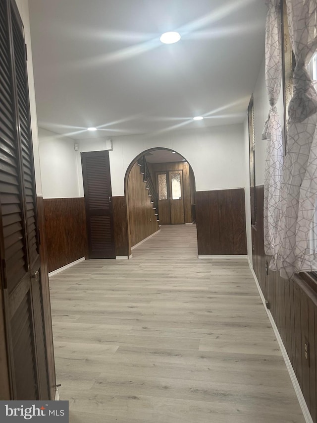 hallway with light wood-type flooring and wooden walls