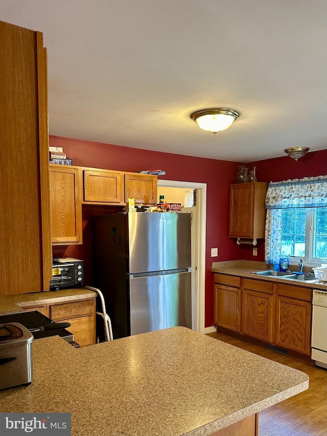 kitchen featuring light wood-type flooring, sink, stainless steel refrigerator, and white dishwasher