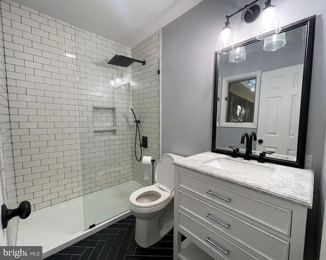 bathroom featuring a tile shower, vanity, and toilet