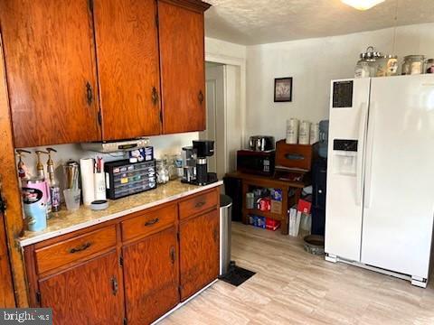 kitchen featuring white refrigerator with ice dispenser, a textured ceiling, and light hardwood / wood-style flooring