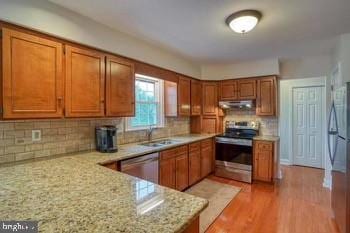 kitchen featuring light stone countertops, sink, stainless steel appliances, tasteful backsplash, and light wood-type flooring