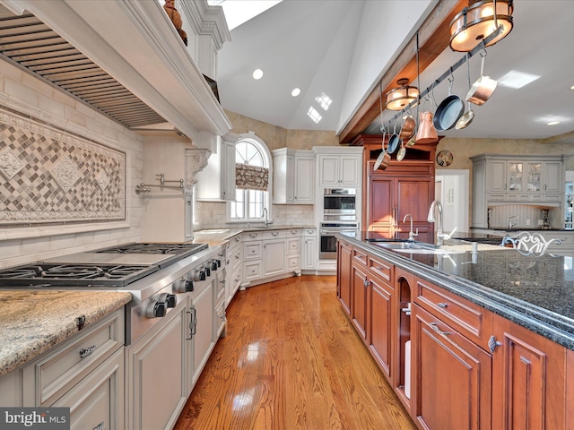 kitchen with decorative backsplash, appliances with stainless steel finishes, vaulted ceiling, white cabinets, and hanging light fixtures