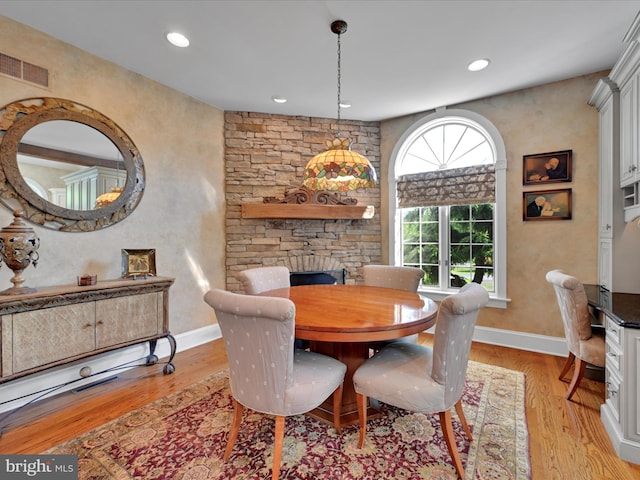 dining room featuring a stone fireplace and light hardwood / wood-style floors