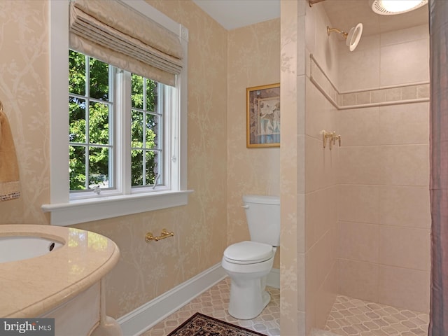 bathroom with tiled shower, tile patterned flooring, toilet, and sink