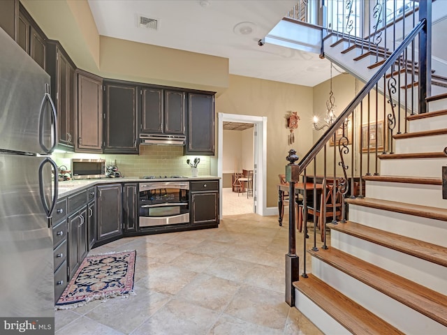 kitchen with tasteful backsplash, dark brown cabinetry, an inviting chandelier, and appliances with stainless steel finishes