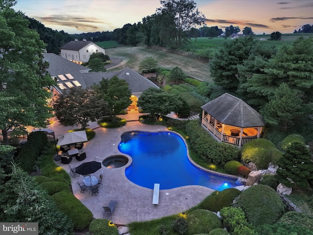 pool at dusk with a gazebo, a diving board, and a patio area