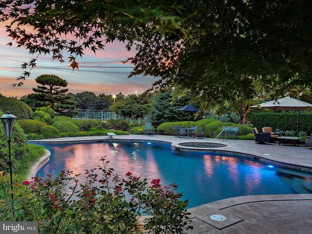 pool at dusk with an in ground hot tub and a patio