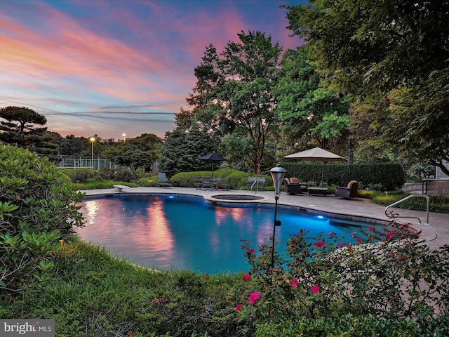 pool at dusk with a patio area, an in ground hot tub, and a diving board