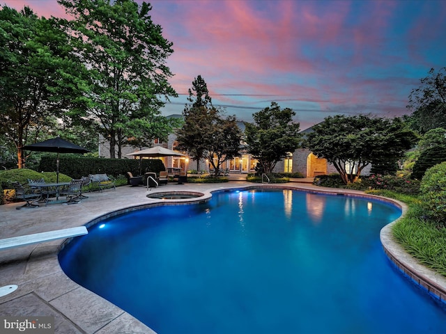 pool at dusk featuring an in ground hot tub, a patio, and a diving board