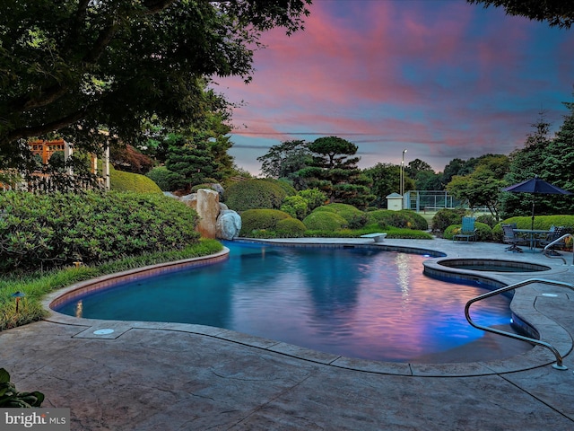 pool at dusk with an in ground hot tub and a diving board