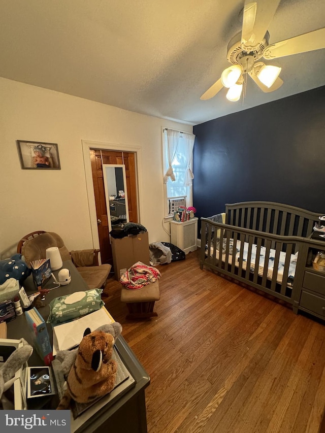 bedroom featuring ceiling fan, wood-type flooring, and a crib