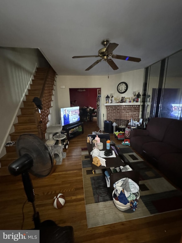 living room featuring ceiling fan, dark hardwood / wood-style flooring, and a brick fireplace