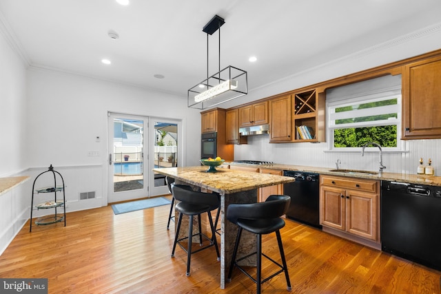 kitchen with sink, a breakfast bar area, wood-type flooring, black appliances, and light stone countertops