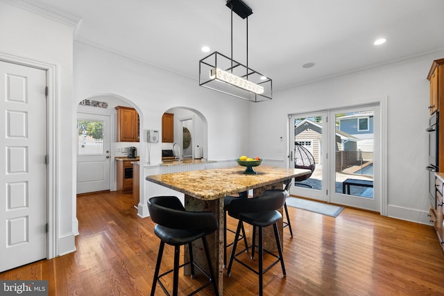 kitchen with a breakfast bar, crown molding, dark hardwood / wood-style flooring, kitchen peninsula, and light stone countertops