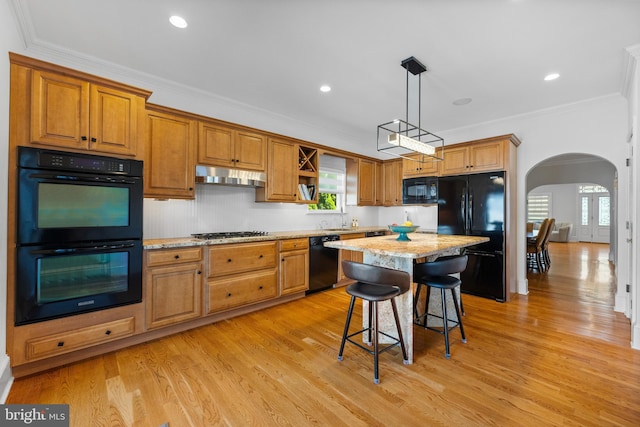 kitchen featuring a kitchen breakfast bar, ornamental molding, a center island, black appliances, and light stone countertops