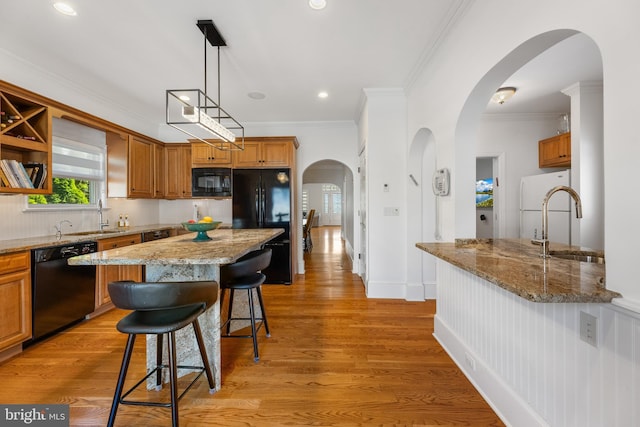 kitchen with crown molding, light stone countertops, a breakfast bar area, and black appliances