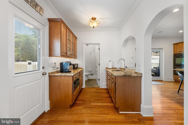 kitchen featuring sink, crown molding, double oven, light stone counters, and light wood-type flooring