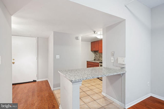 kitchen with light stone countertops, range, tasteful backsplash, kitchen peninsula, and light wood-type flooring