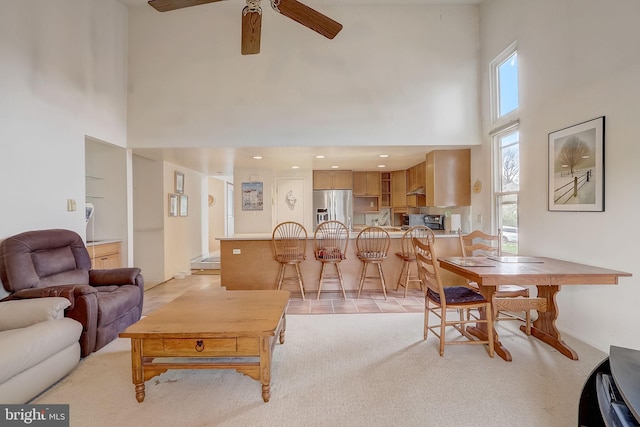 living room featuring ceiling fan, light carpet, and a high ceiling