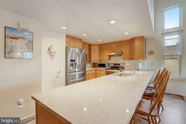 kitchen with kitchen peninsula, appliances with stainless steel finishes, a kitchen breakfast bar, light stone counters, and sink