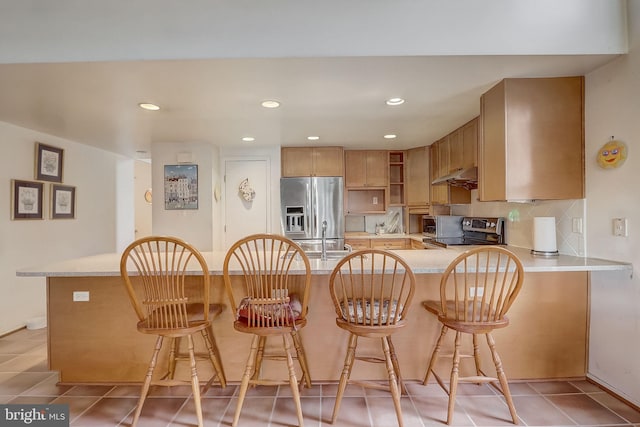 kitchen featuring a breakfast bar, backsplash, appliances with stainless steel finishes, light tile patterned flooring, and kitchen peninsula