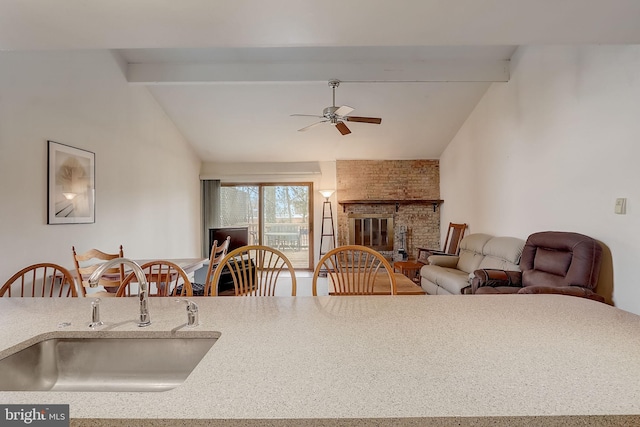 kitchen with vaulted ceiling with beams, ceiling fan, sink, and a fireplace