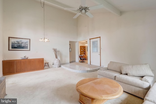 carpeted living room with a towering ceiling, beamed ceiling, and ceiling fan with notable chandelier