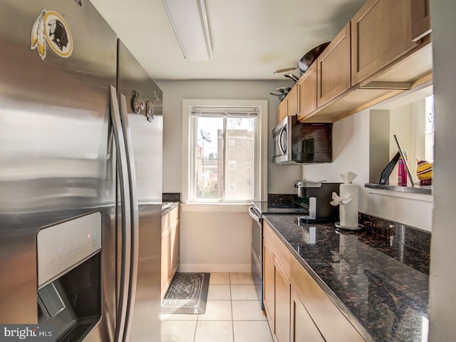 kitchen with light tile patterned flooring, dark stone counters, and appliances with stainless steel finishes