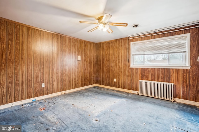 empty room with radiator, ceiling fan, and wood walls