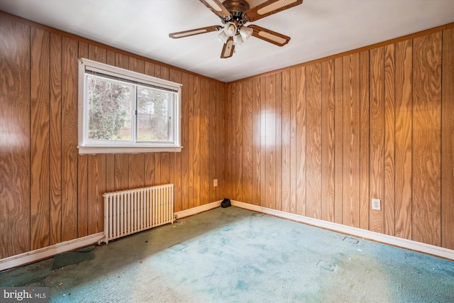 carpeted spare room with radiator heating unit, ceiling fan, and wood walls