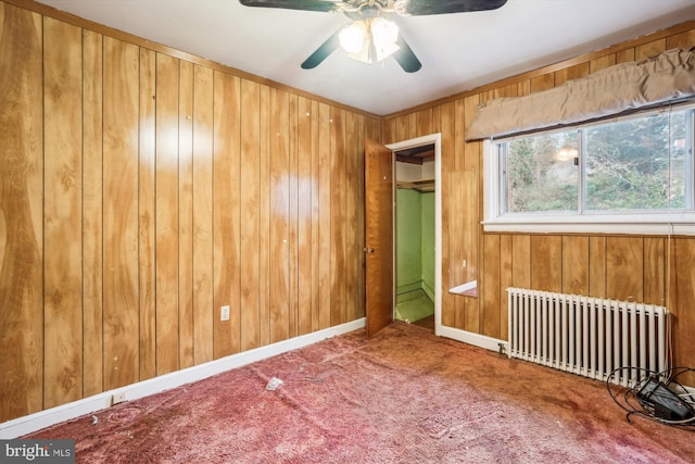 carpeted empty room with radiator, ceiling fan, and wood walls