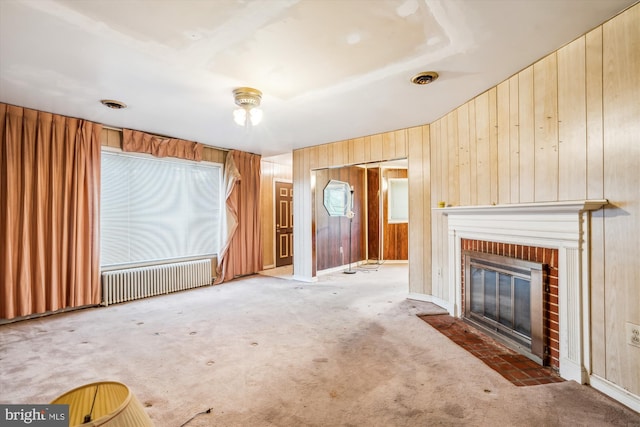 unfurnished living room featuring wooden walls, a fireplace, radiator, and carpet