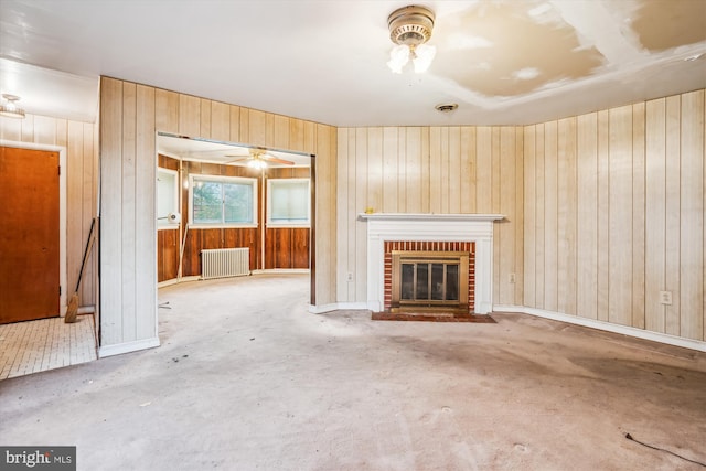 unfurnished living room with ceiling fan, wooden walls, radiator heating unit, and a fireplace