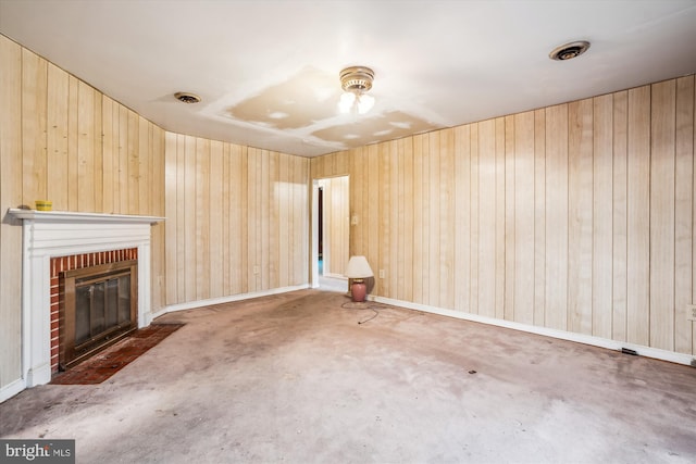 unfurnished living room with wooden walls, concrete flooring, and a brick fireplace