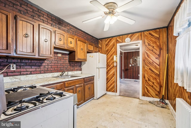 kitchen featuring radiator, white appliances, sink, ceiling fan, and wooden walls