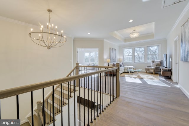 hallway with a raised ceiling, a notable chandelier, crown molding, and light hardwood / wood-style flooring