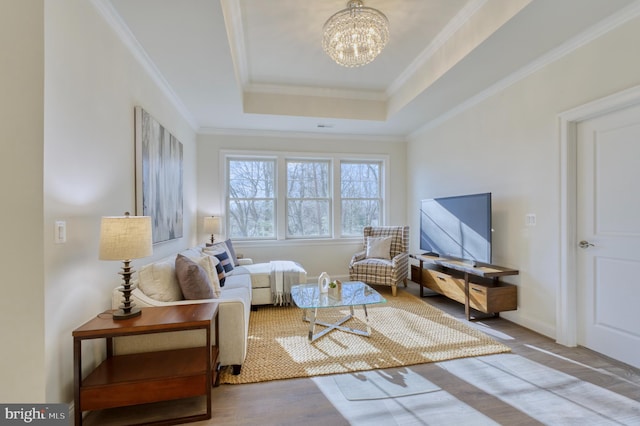 living area featuring hardwood / wood-style flooring, a raised ceiling, a notable chandelier, and crown molding