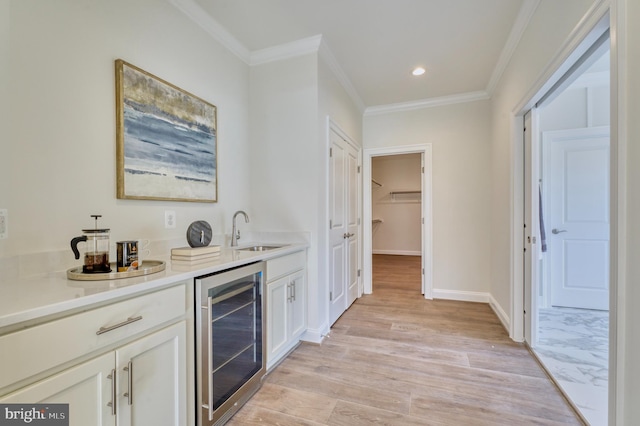 bar with light wood-type flooring, wine cooler, crown molding, white cabinets, and sink