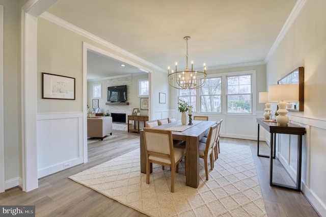 dining room featuring a large fireplace, light wood-type flooring, crown molding, and a notable chandelier